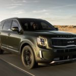 A green 2022 Kia Telluride is shown from the front driving on an open road after leaving a Kia Telluride dealer.