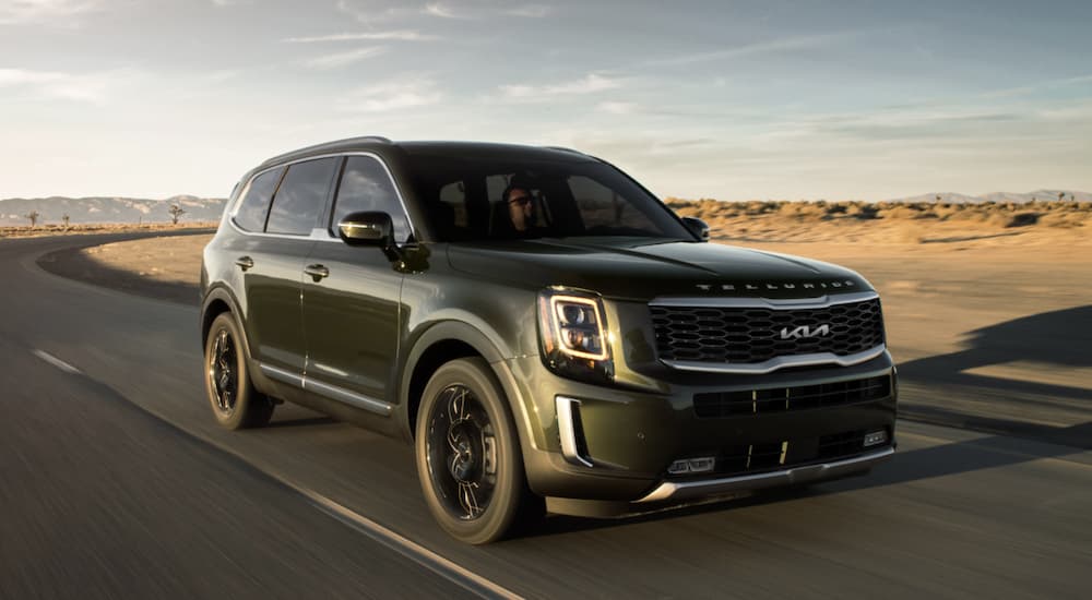 A green 2022 Kia Telluride is shown from the front driving on an open road after leaving a Kia Telluride dealer.