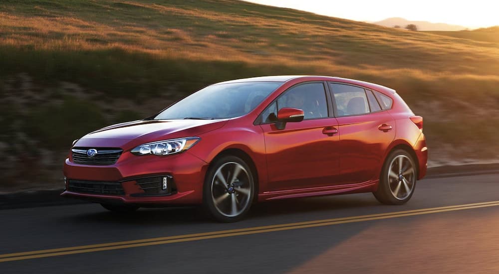 A red 2022 Subaru Impreza Sport is shown from the side driving at sunset after leaving a Subaru dealer.