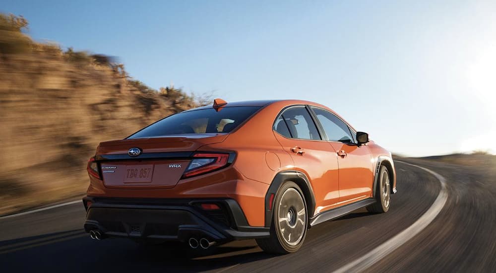 An orange 2022 Subaru WRX Limited is shown from the rear driving on an open road.