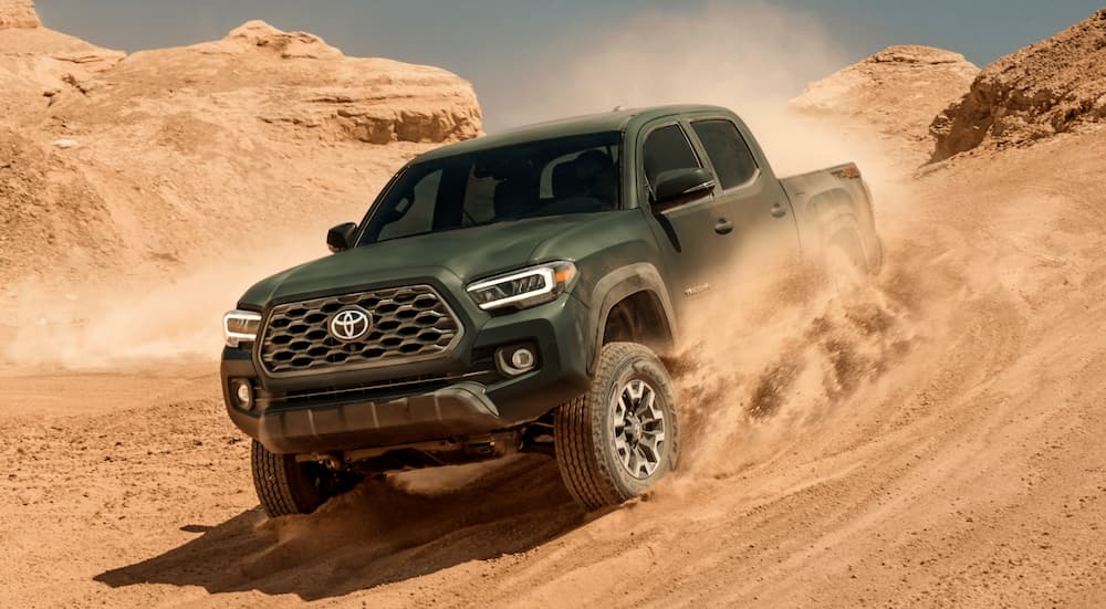 A green 2021 Toyota Tacoma TRD sport is shown from the front while driving through sand.