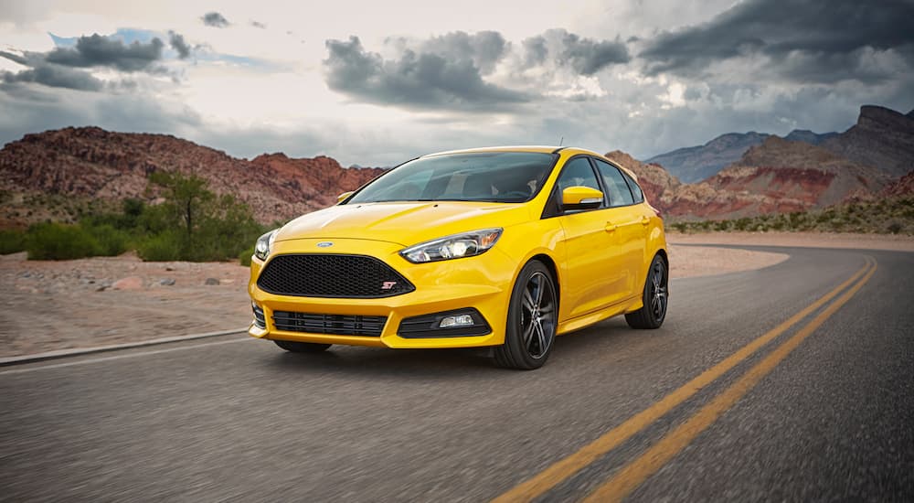A yellow 2017 Ford Focus ST is shown from the front at an angle while it drives down a road.