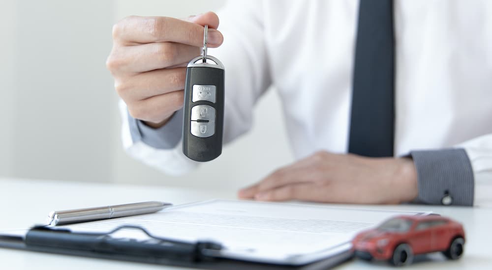 A salesperson is shown holding a car key in front of paperwork and a car key.