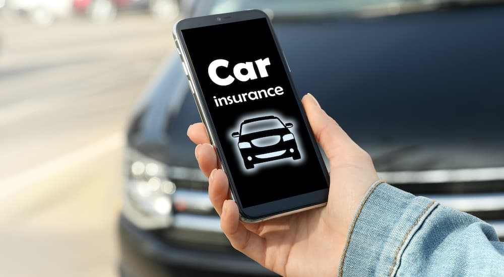 A person is shown holding a phone as they look at their car insurance at an online car dealership. 