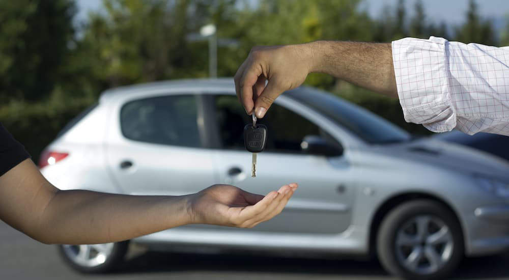 A person is shown passing a key in front of a used car.