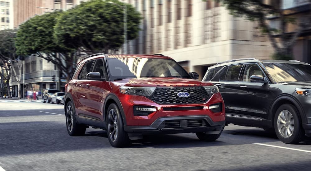 A red 2020 Ford Explorer is shown driving through a city next to a grey 2020 Ford Explorer after searching 'used Ford sales'.