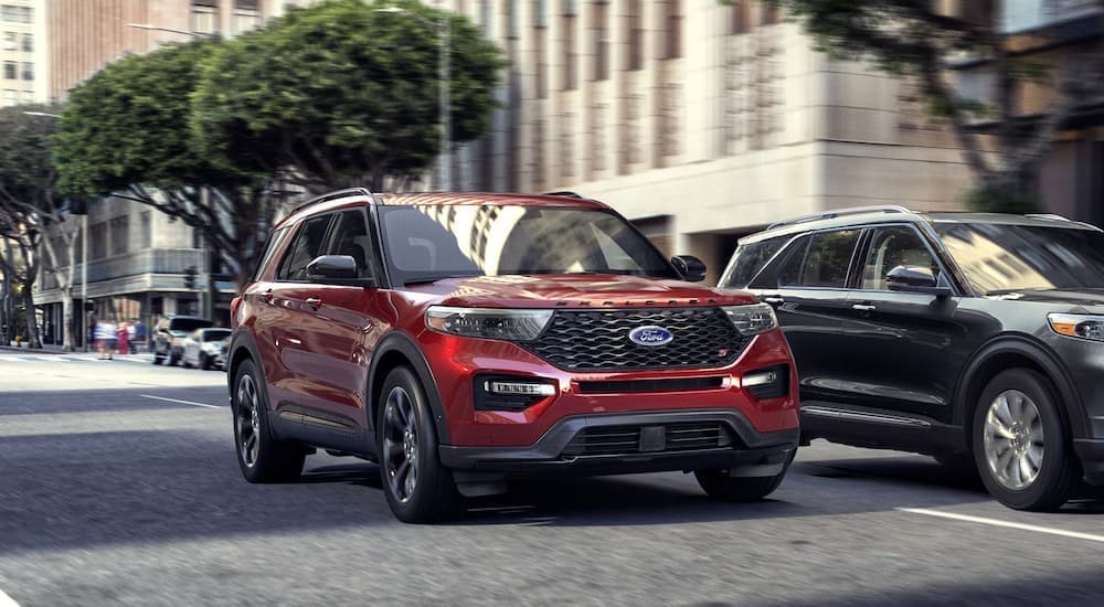A red 2020 Ford Explorer is shown driving through a city next to a grey 2020 Ford Explorer after searching 'used Ford sales'.