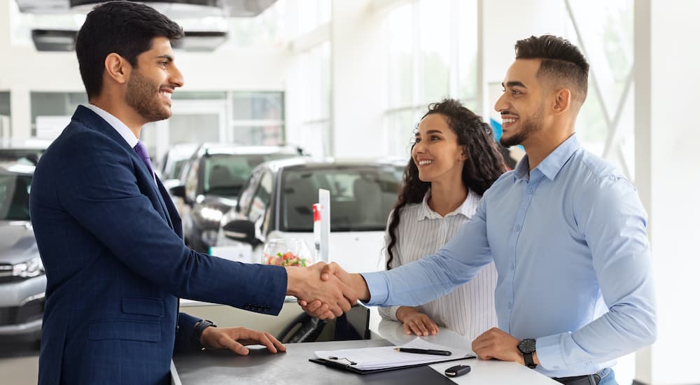 A couple is shown talking to a salesperson at a used car dealership.