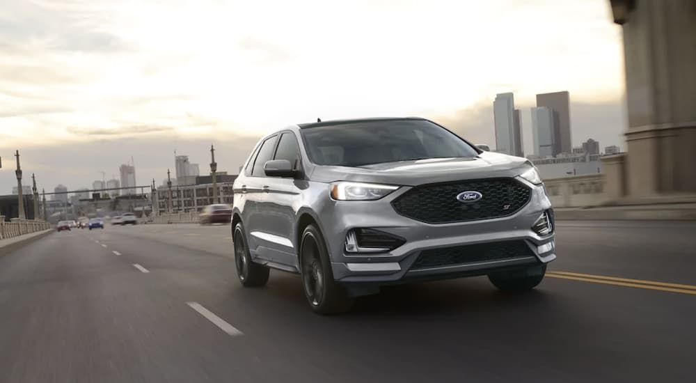 A grey 2022 Ford Edge ST is shown from the front driving past a city.