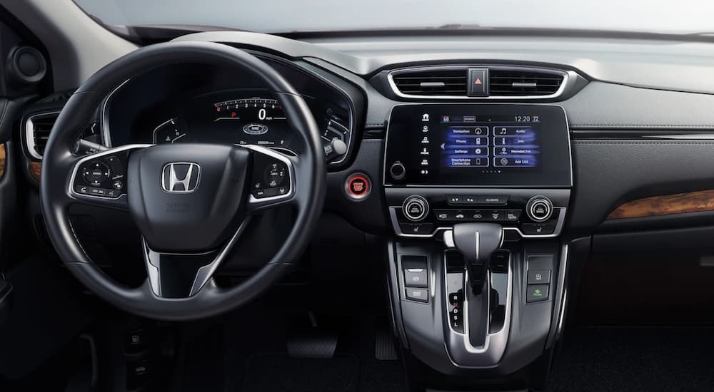 The black interior of a 2022 Honda CR-V Touring shows the steering wheel and infotainment screen.