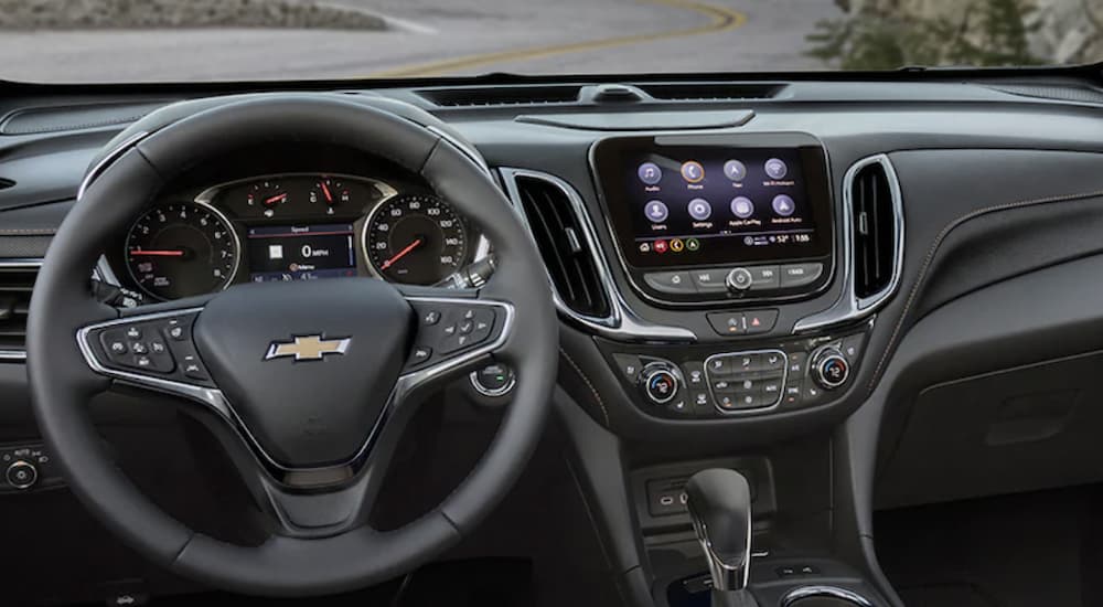The black interior of a 2022 Chevy Equinox shows the steering wheel and infotainment screen during a 2022 Chevy Equinox vs 2022 Honda CR-V comparison.