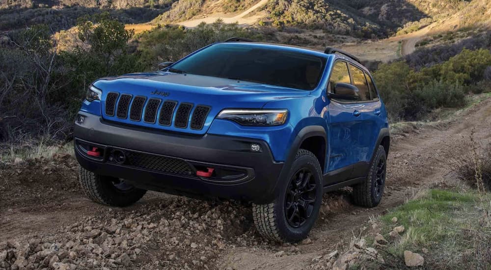 A blue 2022 Jeep Cherokee is shown driving on a dirt road.