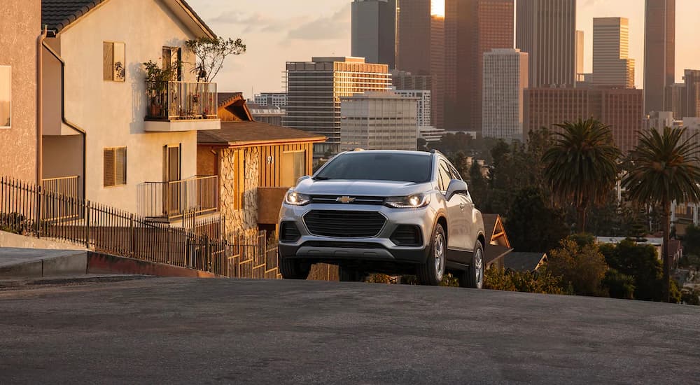 A silver 2022 Chevy Trax is shown driving up a steep city hill.
