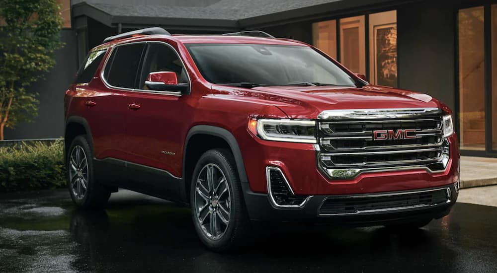 A red 2022 GMC Acadia is shown from the front parked in front of a building during a 2022 GMC Acadia vs 2022 Honda Pilot comparison.