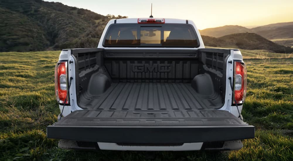 The bed of a white 2022 GMC Canyon is shown parked in a field.