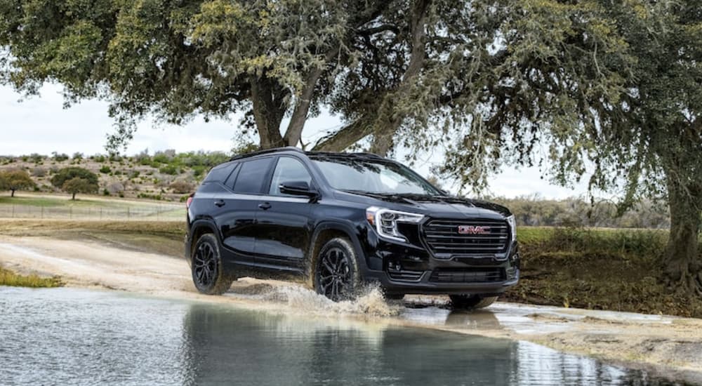 A black 2022 GMC Terrain is shown from the side driving on a dirt road.