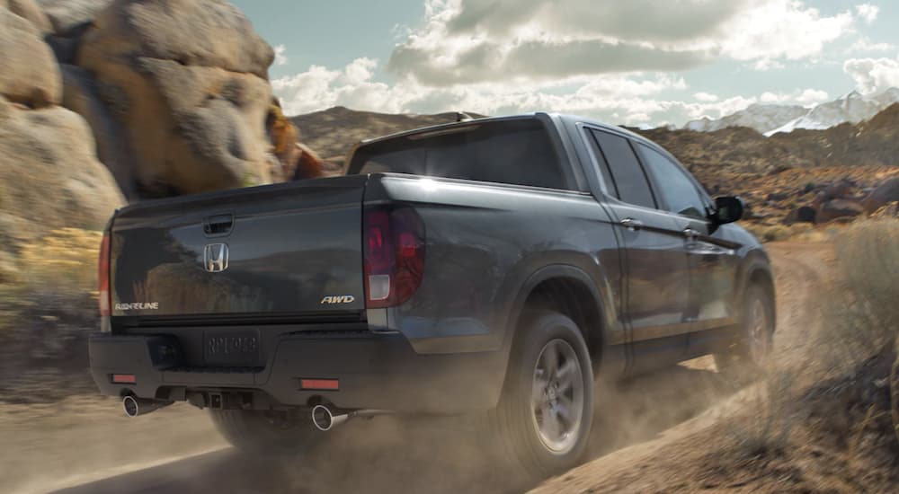 A silver 2022 Honda Ridgeline RTL-E is shown from the rear driving on a dirt road.