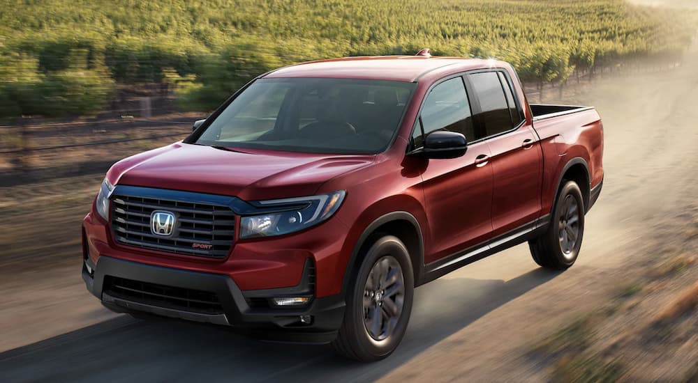 A red 2022 Honda Ridgeline Sport is shown driving on a dirt road during a 2022 Honda Ridgeline vs 2022 Chevy Colorado comparison.