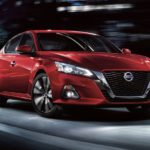 A red 2022 Nissan Altima is shown from the front driving through a city.