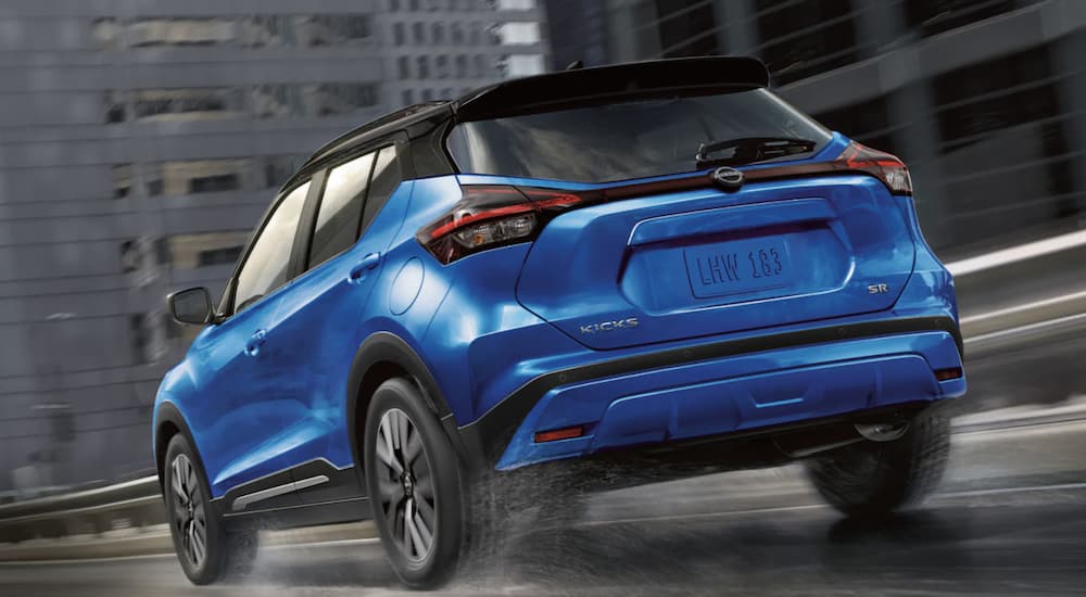A blue 2022 Nissan Kicks is shown from the rear driving through a city.