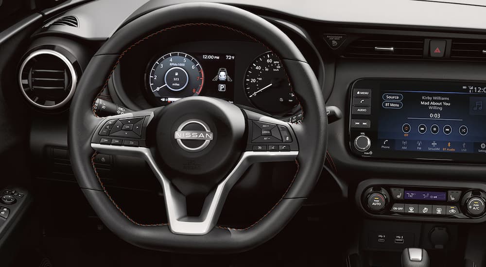 The black interior of a 2022 Nissan Kicks shows the steering wheel and infotainment screen.