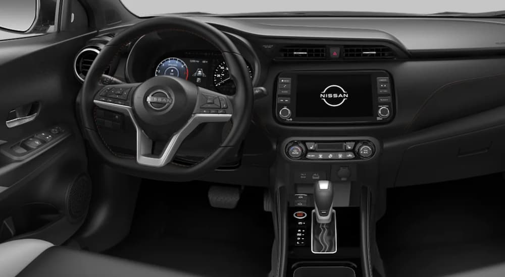 The black interior of a 2022 Nissan Kicks shows the steering wheel and infotainment screen.