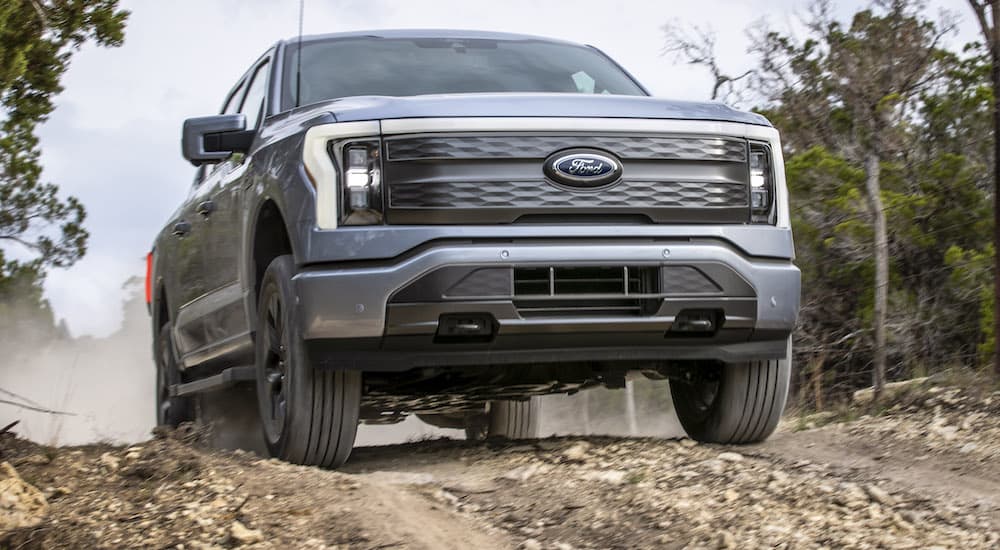 A silver 2022 Ford F-150 Lightning is shown from the front while driving over a dirt hill.