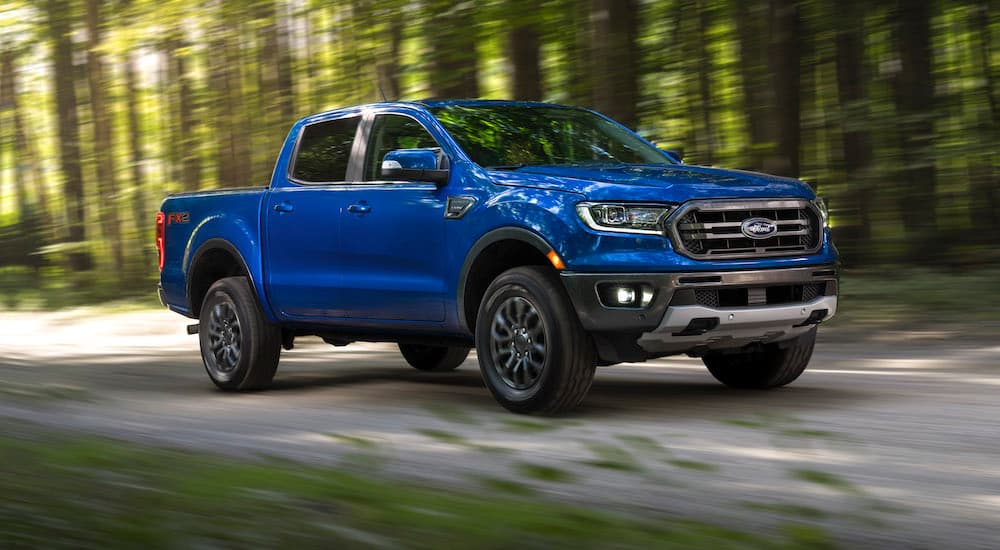 A blue 2022 Ford Ranger is seen from the front at an angle as it drives down a forest trail.