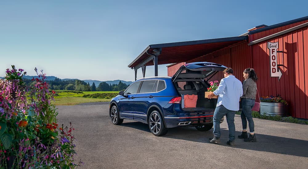 A couple is shown putting supplies in the cargo area of a blue 2022 Volkswagen Tiguan.