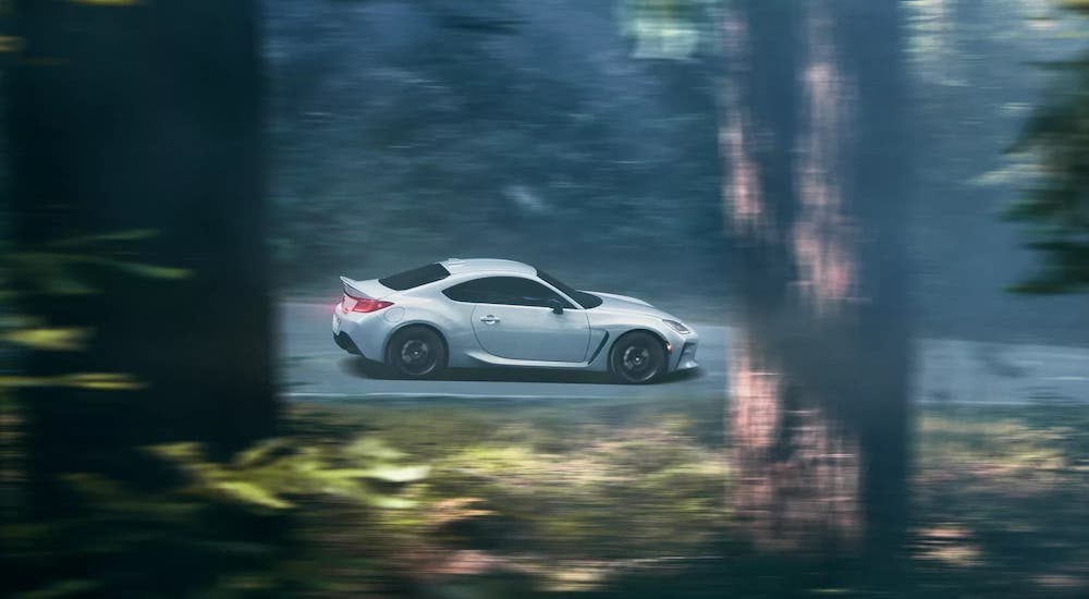 A white 2022 Toyota GR86 is shown from the side while speeding through a forest.