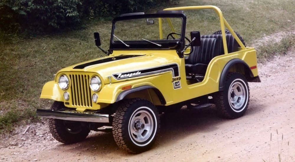 A yellow 1973 Jeep Wrangler is shown from the side driving on a dirt road after searching for 'used Jeep Wrangler for sale.'