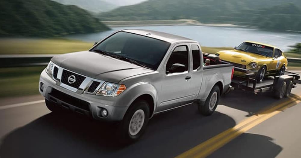 A silver 2020 Nissan Frontier is shown from the front while towing a Datsun 280z.
