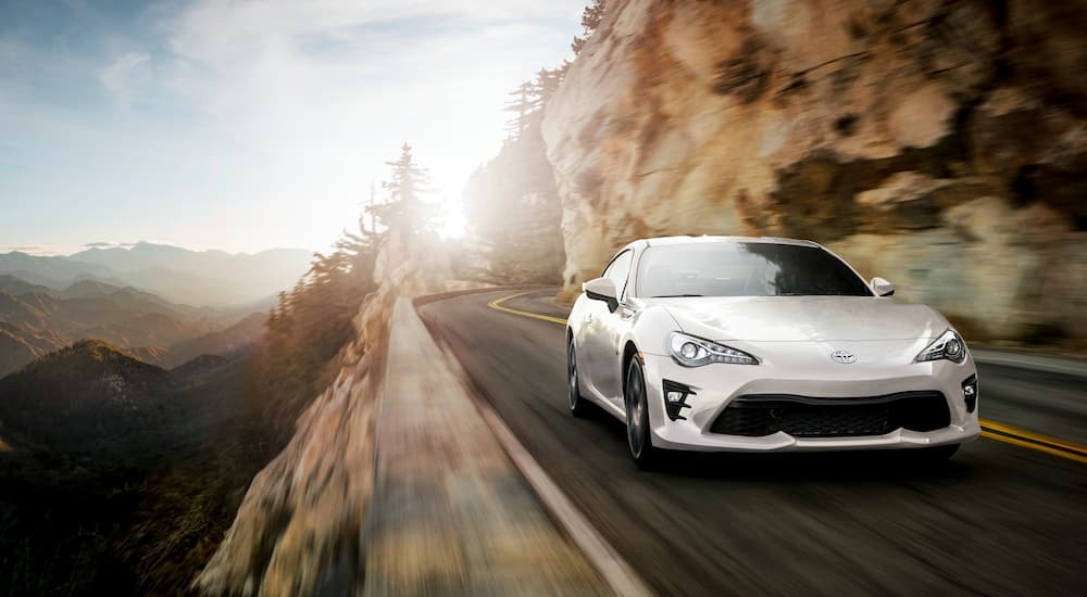 A white 2020 Toyota GT86 is shown from the front while driving down the road after the owner searched 'used car dealer'.