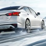 A white 2022 Nissan Altima is shown from the rear on a snowy road after leaving a Nissan dealer.