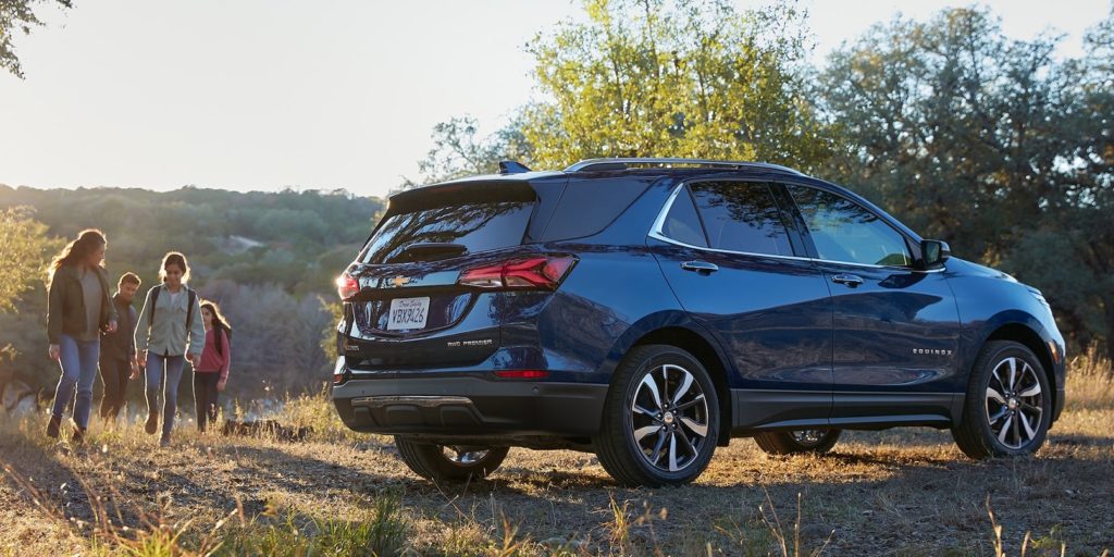 A blue 2022 Chevy Equinox is shown from the side parked near a hiking trail.