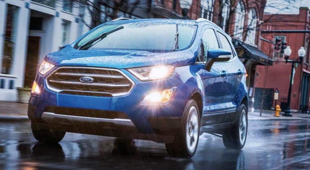 A blue 2022 Ford EcoSport is shown from the front driving through a city in the rain.