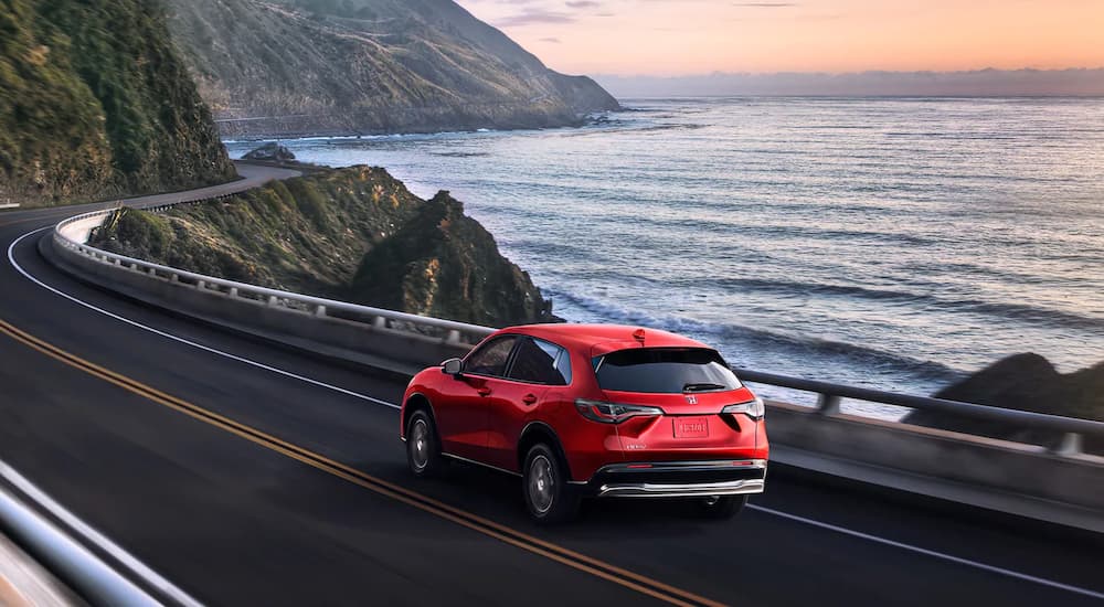 A red 2023 Honda HR-V EX-L is shown from the rear driving on a coastal road.