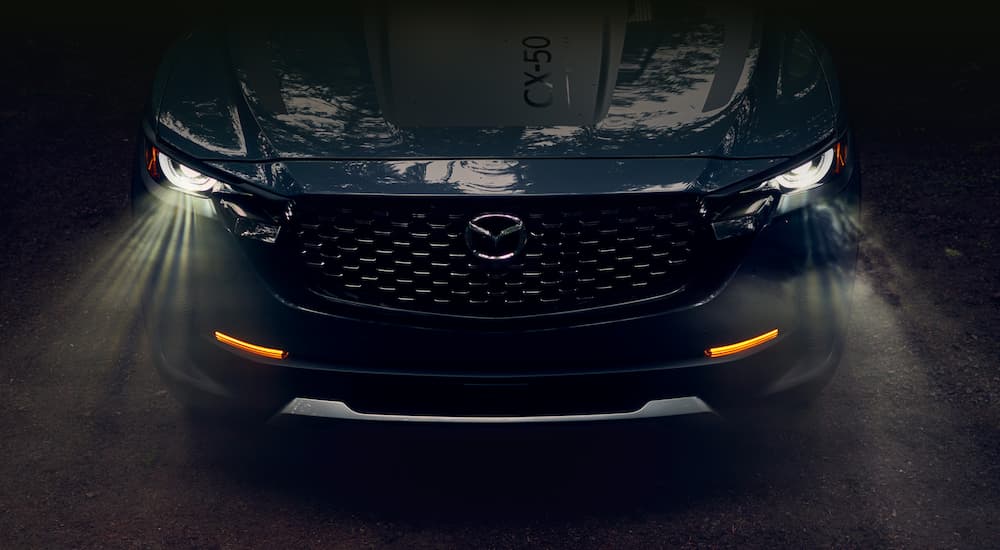A close up shows the front end and illuminated headlights on a dark blue 2023 Mazda CX-50.