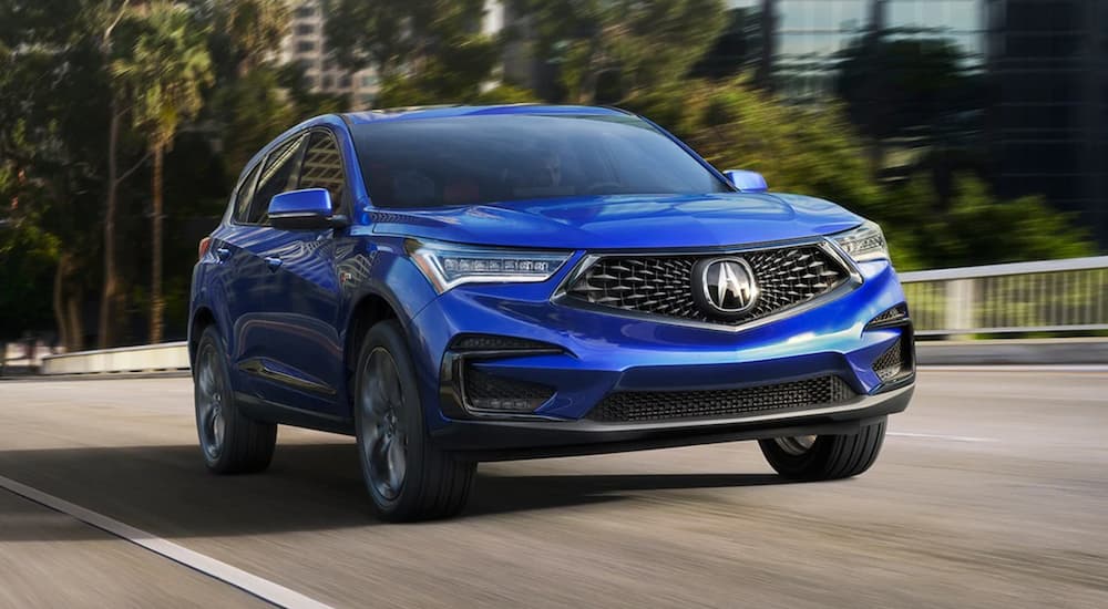 A blue 2021 Acura RDX is shown driving down a city street.