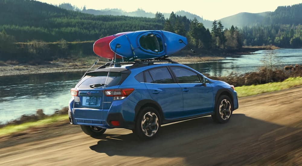 A blue 2022 Subaru Crosstrek Limited is shown driving past a river with kayaks on the roof.
