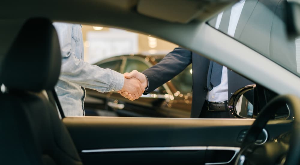 Two people are shown shaking hands next to a car window.