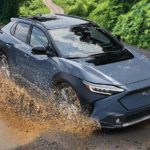 A blue 2023 Subaru Solterra is shown driving through a mud puddle.