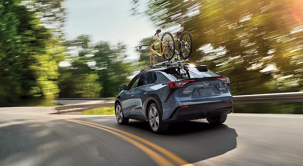 A blue 2023 Subaru Solterra is shown from the rear driving on a road curve.