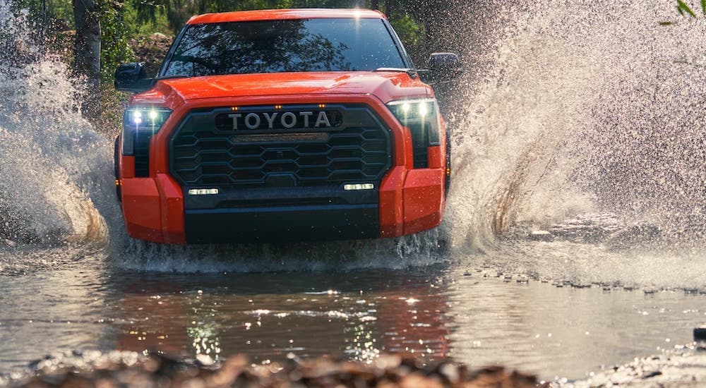 An orange 2022 Toyota Tundra is shown from the front while driving through water.