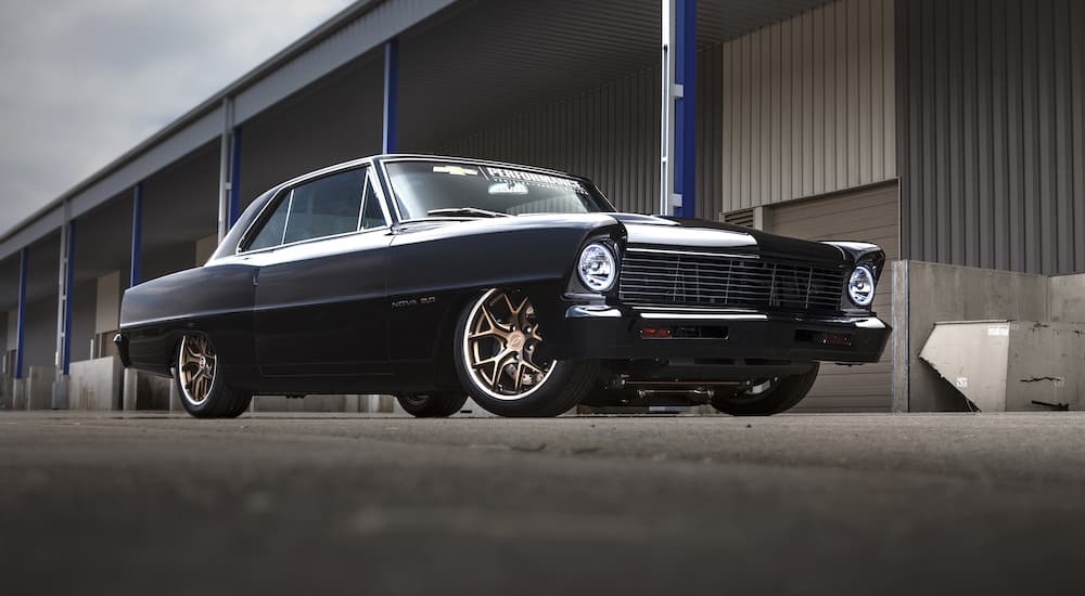 A black 1967 Chevy Nova is shown parked in front of a warehouse.