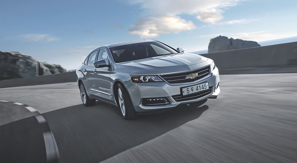 A silver 2016 Chevy Impala is shown driving on a coastal road after visiting a used Chevy dealership.