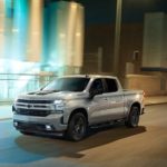 A Certified Pre-Owned silver 2020 Chevy Silverado 1500 Rally Edition is shown from the front at an angle while driving though a city at night.