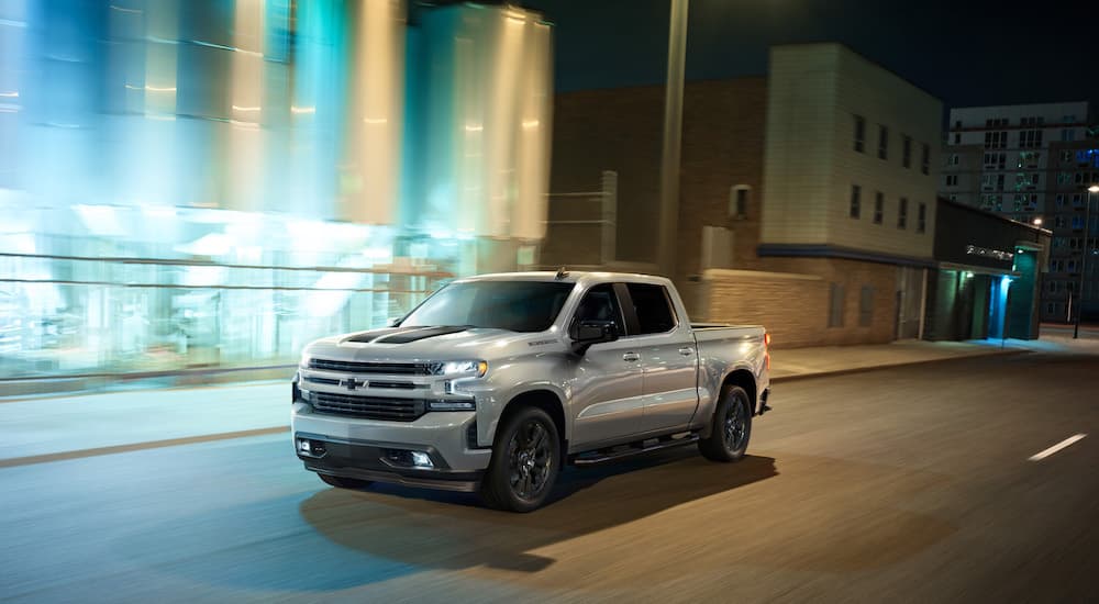 A Certified Pre-Owned silver 2020 Chevy Silverado 1500 Rally Edition is shown from the front at an angle while driving though a city at night.