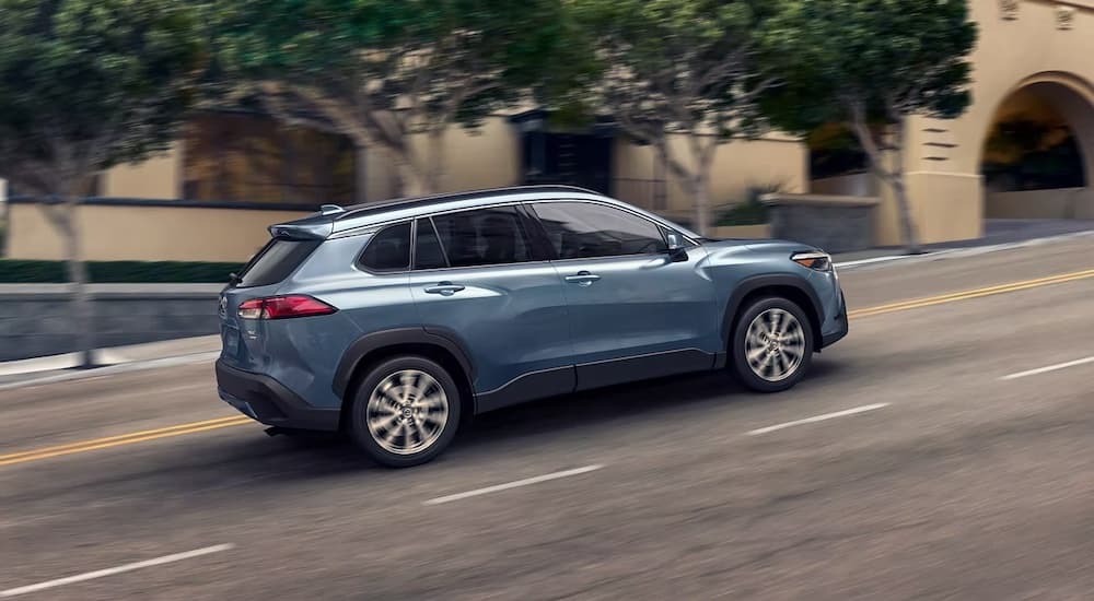 A blue 2023 Toyota Corolla Cross Hybrid is shown from the side while driving up a hill.