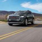 A grey 2022 GMC Acadia Denali is shown driving on an open road.